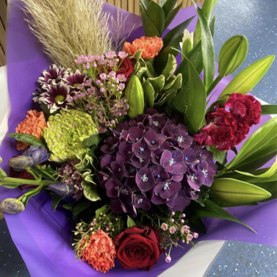 Out in the Woods - A enchanting handtied bouquet in water presented in a gift box/bag. Created using purple, red and peach flowers with complimentary foliage. Hand delivered with care in and around Newcastle by Fantasia Florist.